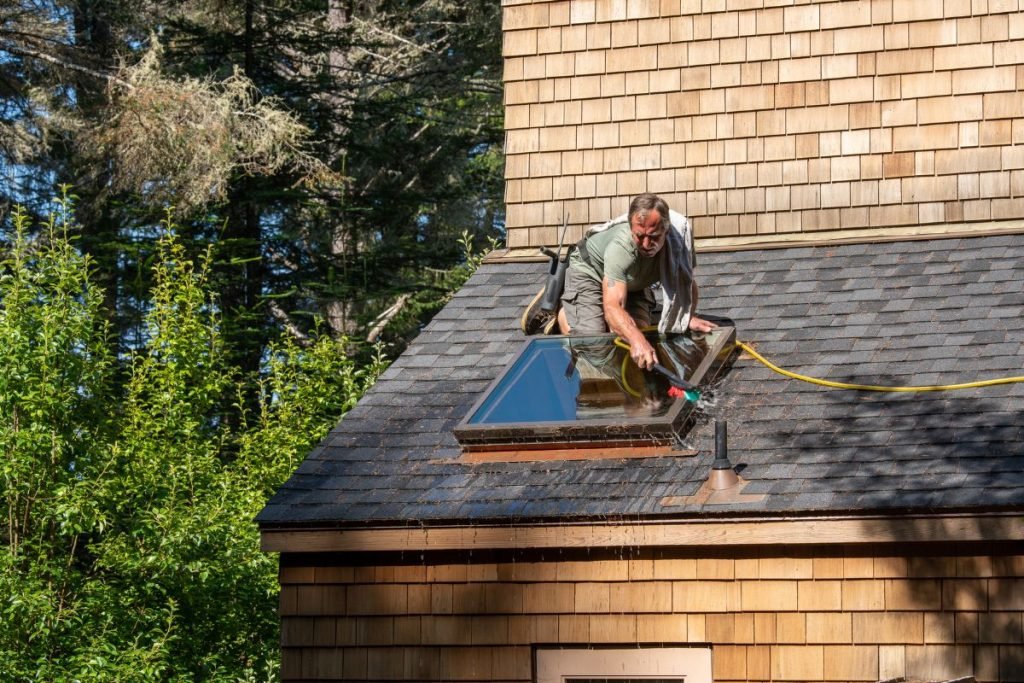 A man is diligently working on a roof, focused on his task amidst a clear blue sky.