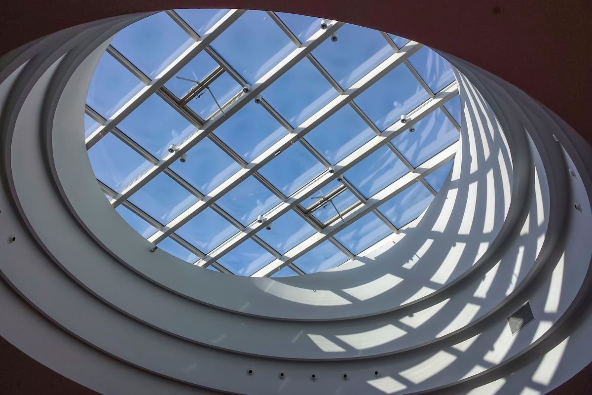  A circular skylight in a building, framed by a clear blue sky above, allowing natural light to illuminate the interior. 
