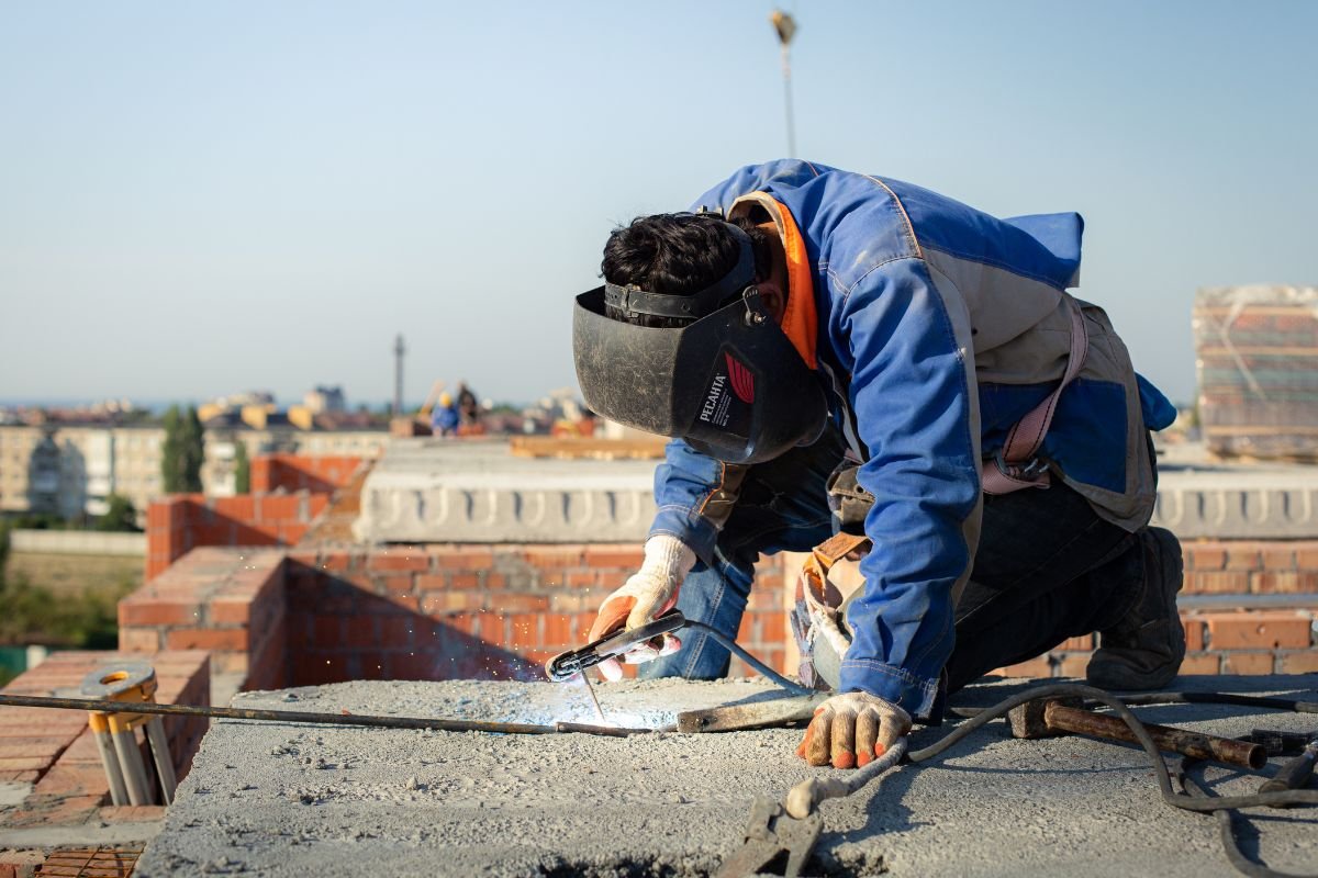 A man in a blue jacket welding on a brick, focused on skylight maintenance and care.